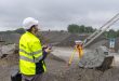 Construction worker operating a drone at a gravel quarry site with surveying equipment in the foreground.