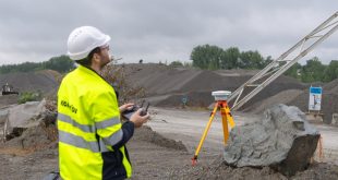 Construction worker operating a drone at a gravel quarry site with surveying equipment in the foreground.