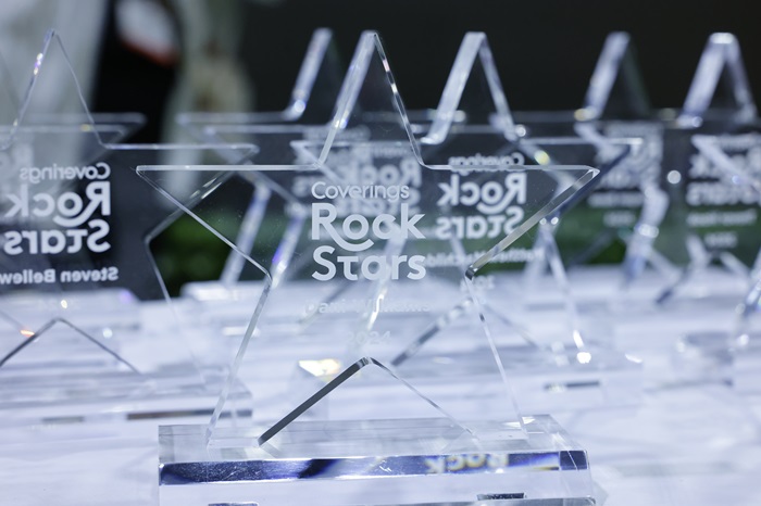 Transparent glass star-shaped awards engraved with "Coverings Rock Stars" are arranged on a table.