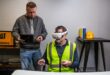 Worker using CAT simulator training with VR headset and controllers in a construction environment.