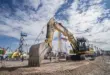 Large Caterpillar excavator on display at the Samoter 2023 fair under a partly cloudy sky, surrounded by construction machinery and cranes.