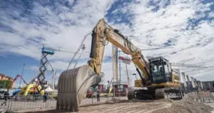 Large Caterpillar excavator on display at the Samoter 2023 fair under a partly cloudy sky, surrounded by construction machinery and cranes.
