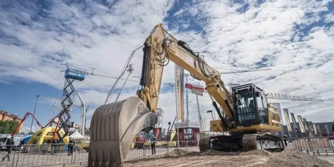 Large Caterpillar excavator on display at the Samoter 2023 fair under a partly cloudy sky, surrounded by construction machinery and cranes.