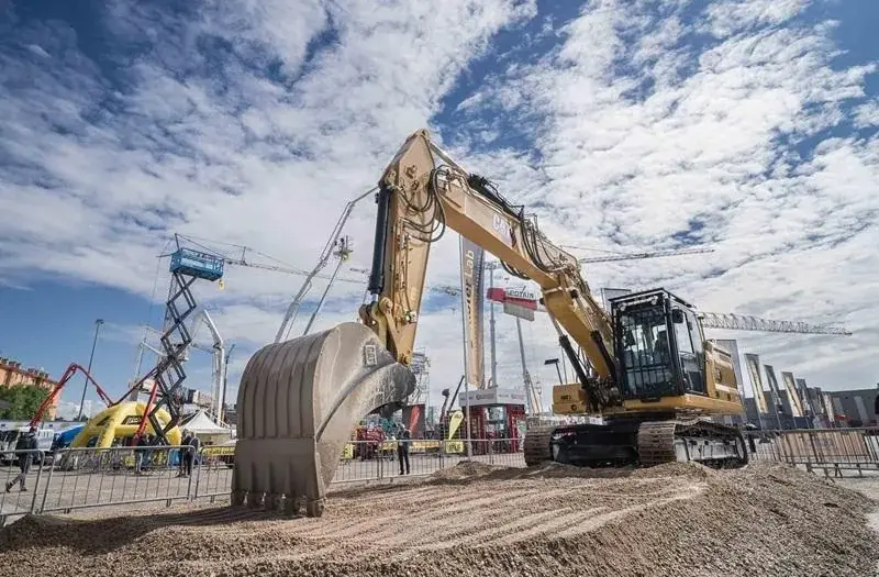 Large Caterpillar excavator on display at the Samoter 2023 fair under a partly cloudy sky, surrounded by construction machinery and cranes.